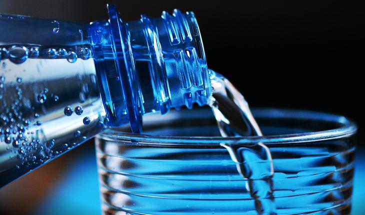 garrafa de água de plástico azulado derramendo água em um copo de vidro