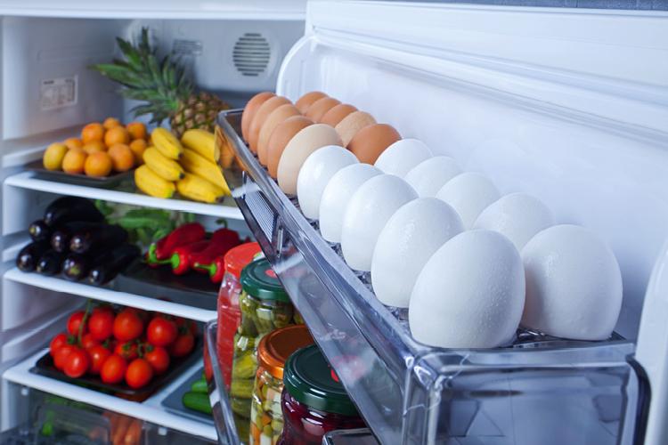geladeira em ordem aberta com ovos na porta e frutas nas prateleiras