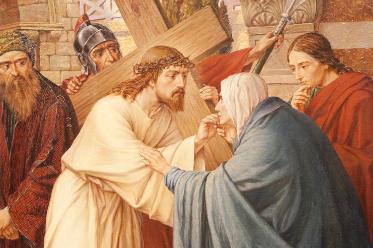 Jesus carregando uma cruz sobre os ombros e conversando com uma mulher. Pessoas ao fundo observando.