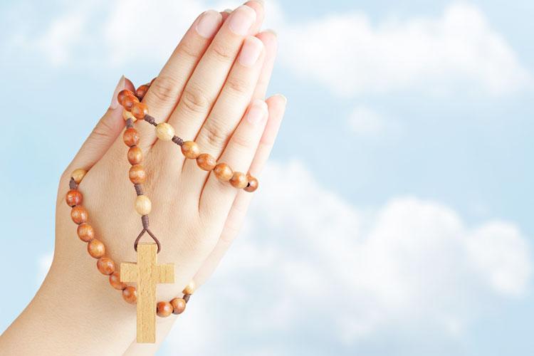 Mãos segurando um terços em sinal de oração