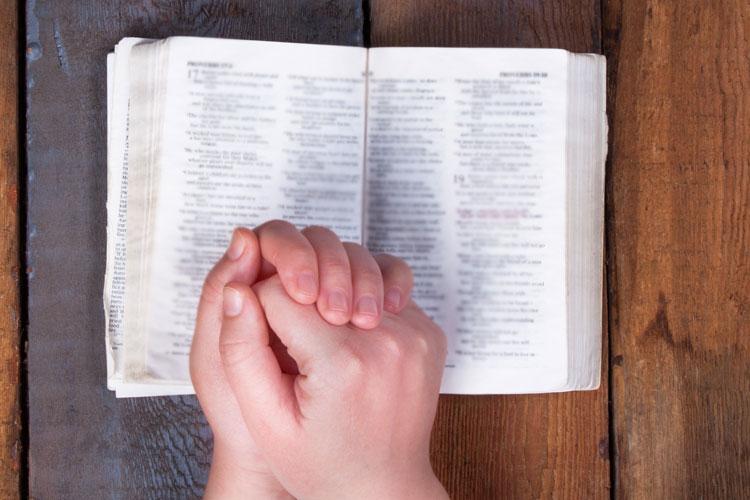 Mãos juntas sobre uma Bíblia aberta