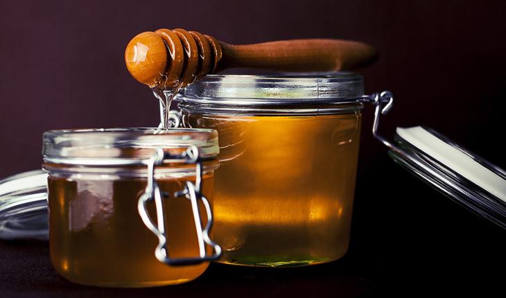 dois potes de vidro cheios de mel com o pegador de mel sobre eles