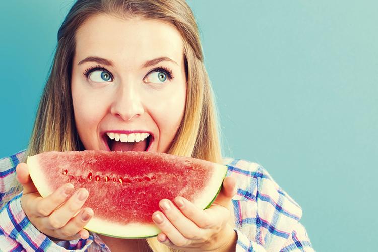 Menina loira comendo um pedaço de melancia, alimento com calorias negativas, e sorrindo