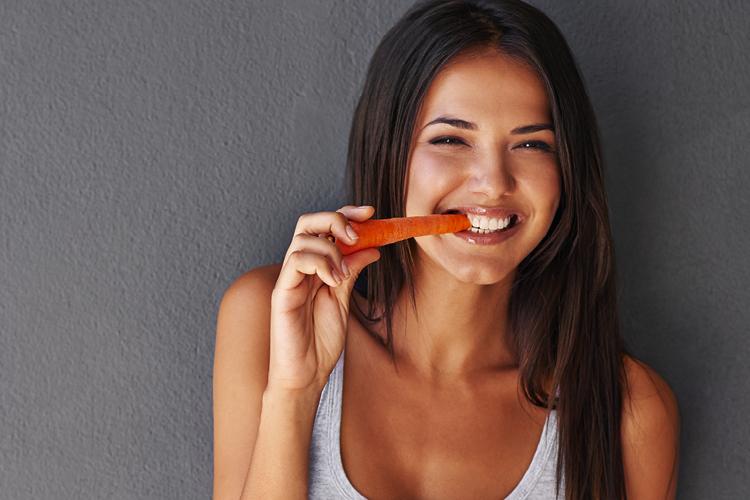 Moça sorrindo para a foto comendo cenoura a fim de manter a glicemia controlada
