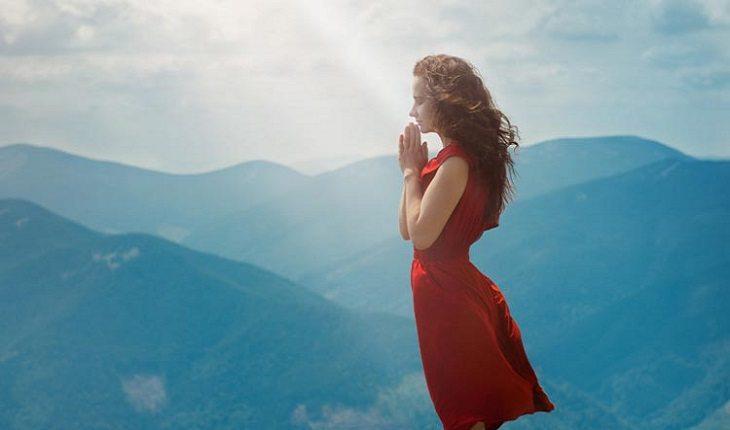 mulher rezando em pé em uma montanha