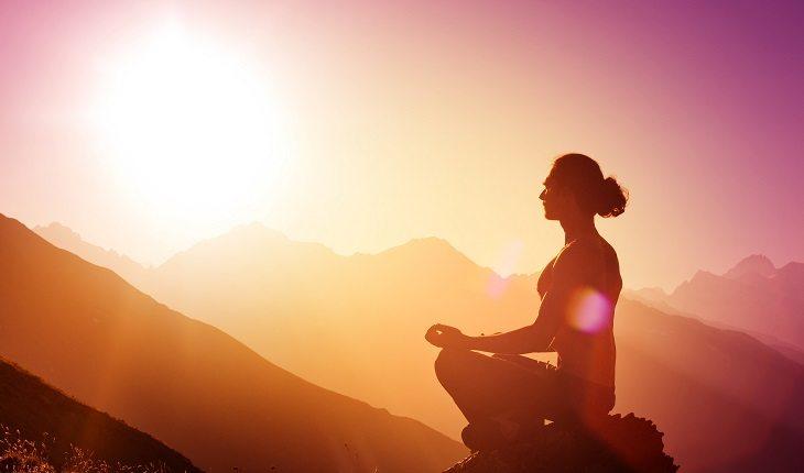 mulher meditando em uma montanha com o sol ao fundo