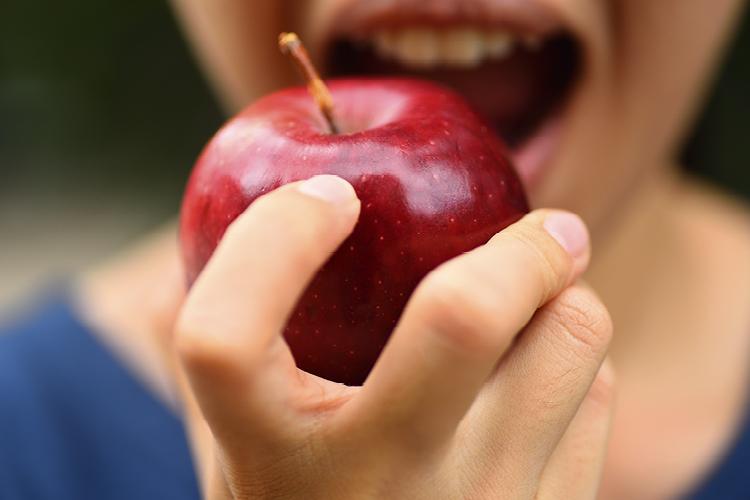 Mão de uma mulher segurando uma maçã e sua boca aberta pronta para morder