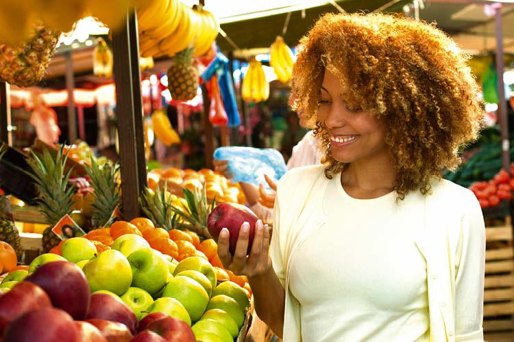 Mulher negra sorrindo escolhendo frutas em uma feira ao ar livre