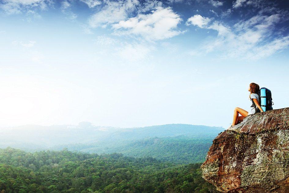 mulher observando paisagem sentada no pico de uma montanha com uma mochila nas costas
