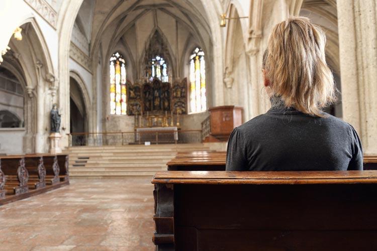 Mulher rezando em uma igreja com o altar ao fundo