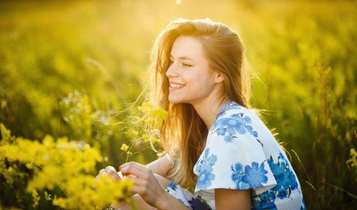 A foto mostra uma mulher sentada em um campo sorrindo com a luz do sol em seu rosto