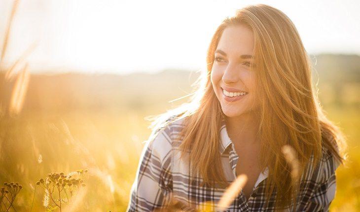 A foto mostra uma mulher sorrindo sentada em um campo