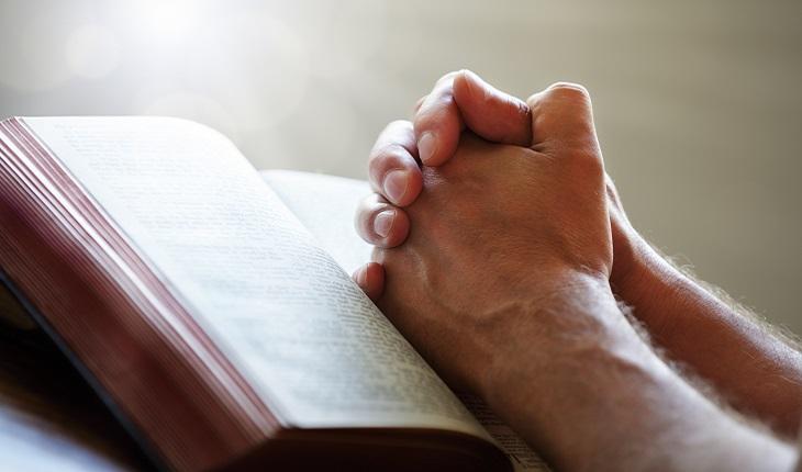 A foto mostra uma pessoa apoiada em uma Bíblia rezando para o processo de exorcismo