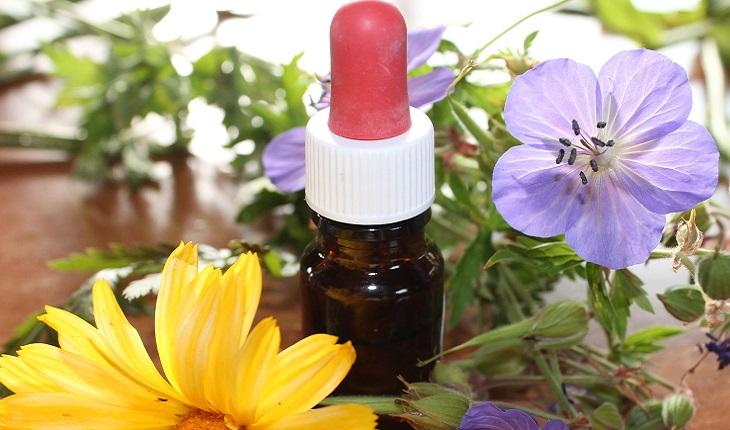 A foto mostra um frasco de homeopatia rodeado por flores
