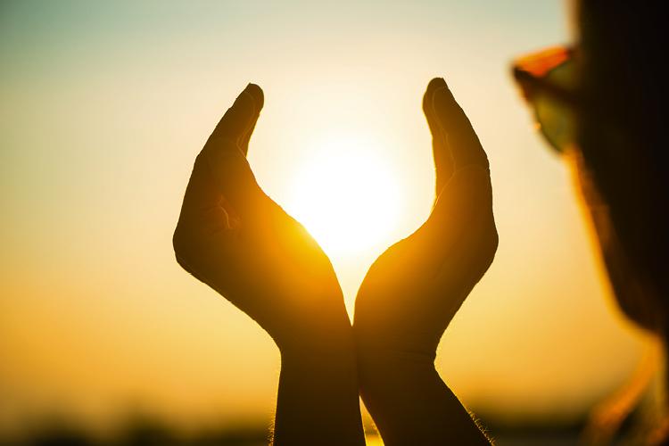 Mulher apreciando o pôr do sol com as mãos recebendo a poderosa vitamina D