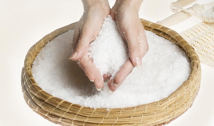 mão de mulher segurando uma quantidade de sal grosso sobre uma tigela cheia de sal grosso