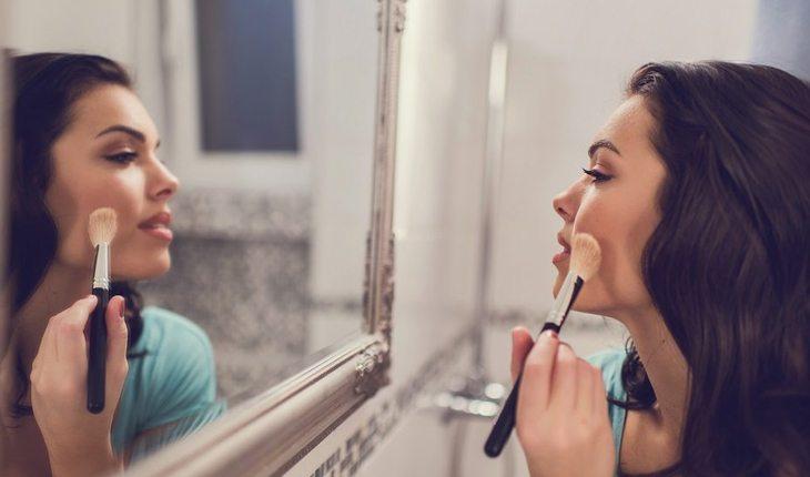 mulher passando blush olhando para o espelho