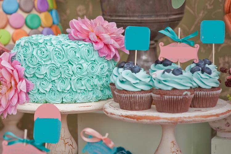 mesa de festa com bolo decorado com glacê azul, cupcakes de massa de chocolate com glacê azul e topers