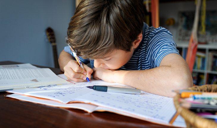 criança em uma mesa estudando e escrevendo no caderno
