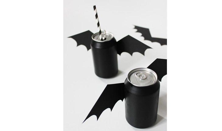 Na foto há uma ideia de decoração de Halloween com latas de refrigerante com asas de morcego.