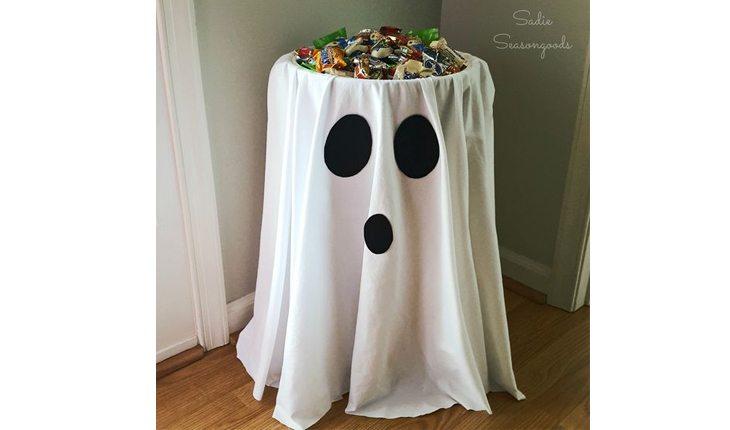 Na foto há uma ideia de decoração de Halloween com uma mesa de doces com um pano branco, formando um fantasma.