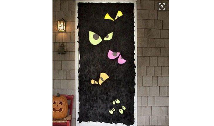 Na foto há uma ideia de decoração de Halloween com uma porta revestida com crepon preto e caretas coloridas.