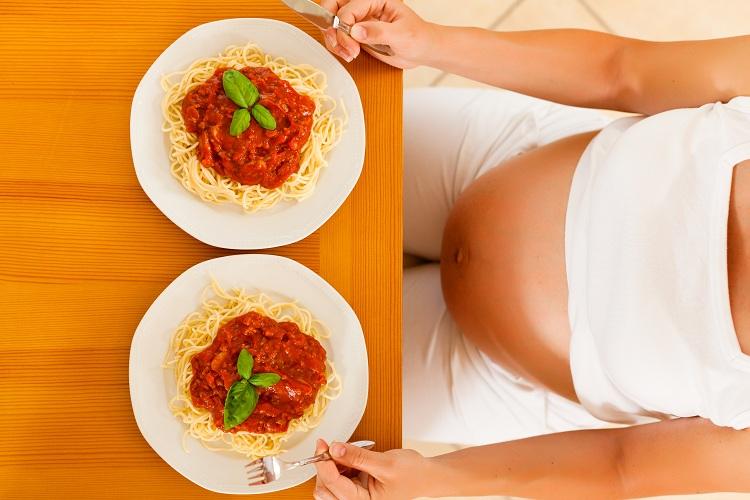 grávida sentada à mesa com dois pratos de macarrão