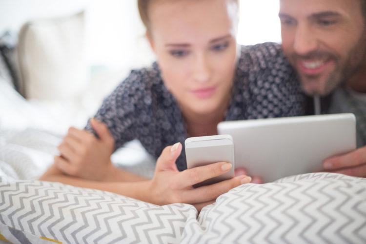 homem-mulher-deitaidos-cama-digitando-tablet-smartphone-apple-iOS 10-conversando-sorrindo