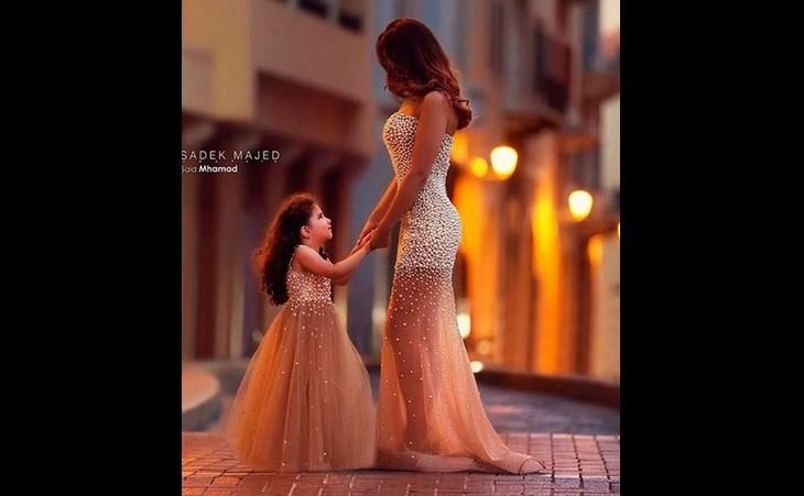 Mulher e filha pequena se dão as mãos em um ambiente urbano enquanto anoitece, as duas estão com um vestido tie-dye