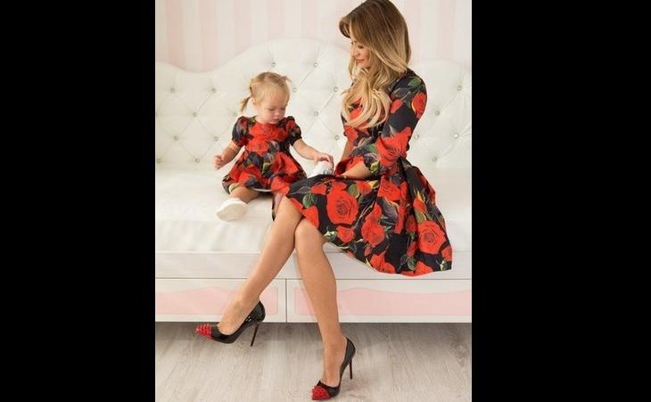 Mãe e filha bebê sentadas em um sofá, as duas estão usando vestidos floridos