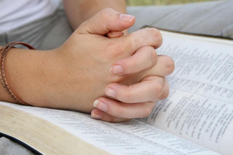 Mãos em posição de oração sobre uma Bíblia aberta
