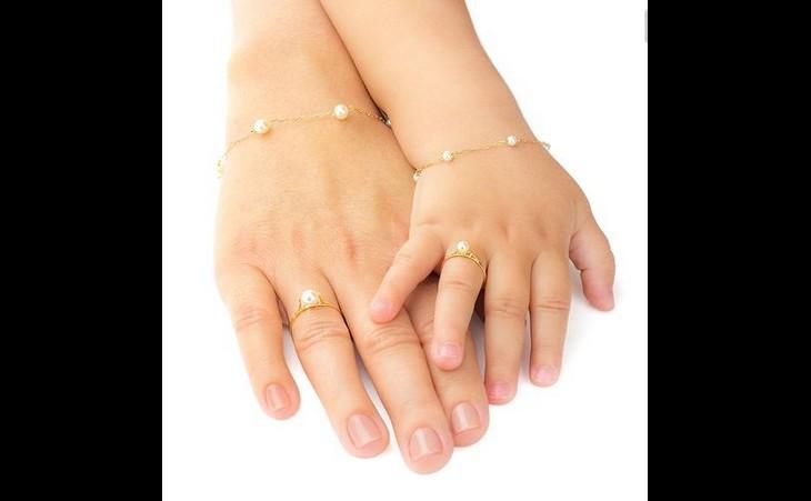 Duas mãos, de mãe e filha, com os mesmos acessórios dourados na pulseira e anel