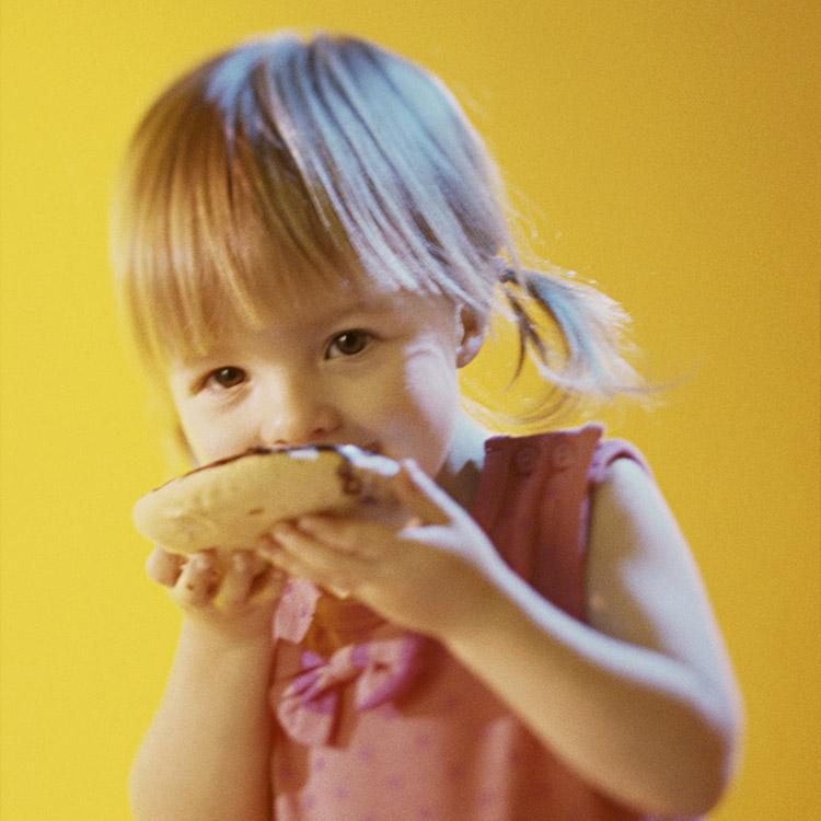 menina comendo doce com fundo amarelo