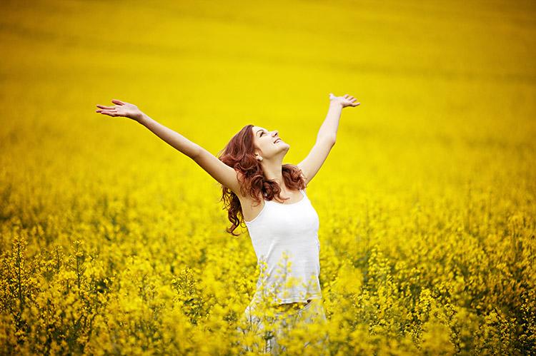 Mulher sozinha e feliz, com os braços abertos, em um campo de flores amarelas