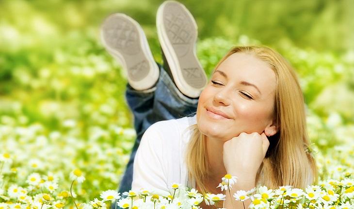Na imagem há uma mulher deitada de bruços em um campo florido sorrindo. Dar risada ajuda a melhorar a respiração