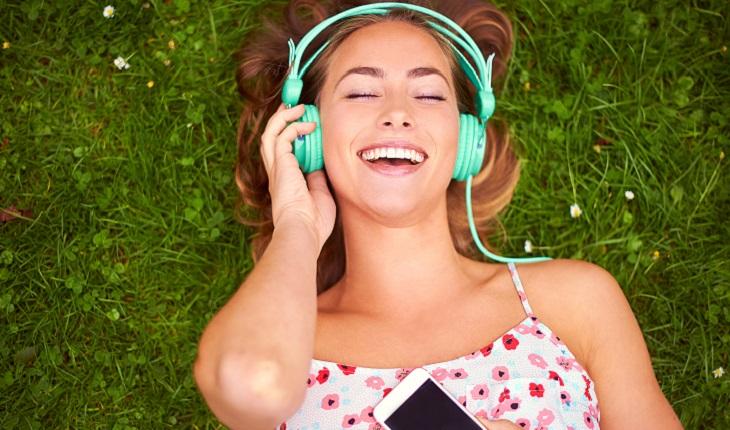 A foto mostra uma garota deitada em um gramado ouvindo música de olhos fechados, uma prática importante para desenvovler o cérebro de uma mulher multitarefas