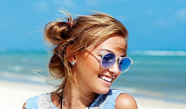 Mulher sorridente de óculos azuis na praia