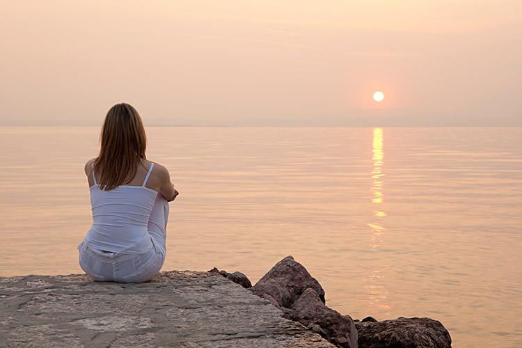 mulher sentada na pedra vendo o por do sol no mar