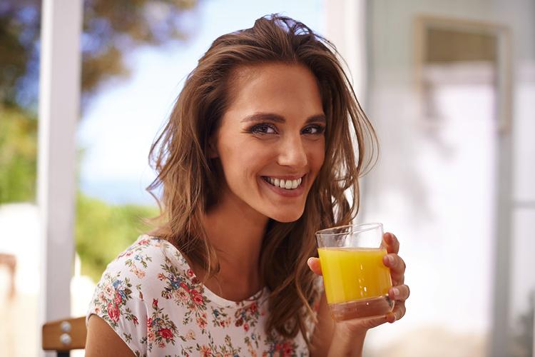 mulher sorrindo bebendo suco de laranja