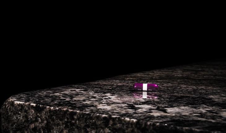 Em cima de uma bancada de granito está uma pílula rosa quase lilás. Falhas no anticoncepcional.