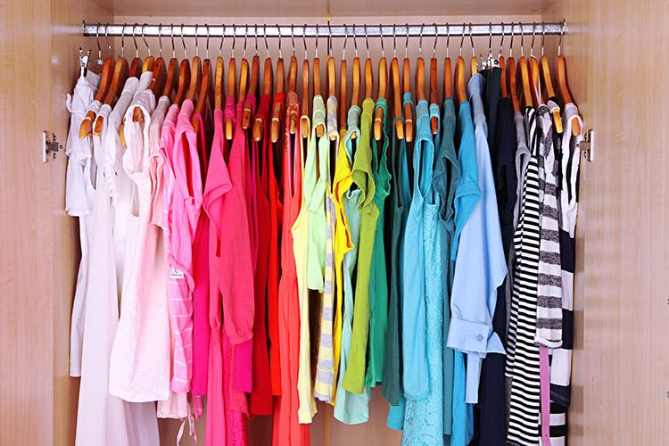 várias roupas coloridas e organizadas por cor dentro de um guardaroupa, penduradas no cabide