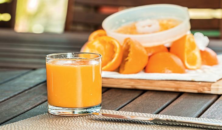 suco de laranja em um copo de vidro e um espremedor com algumas laranjas espremidas