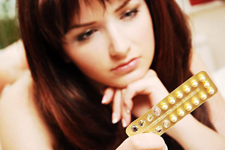 mulher olhando para uma cartela de anticoncepcional 