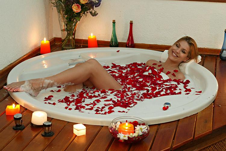 mulher tomando banho na banheira, cheia de pétalas de rosa e velas em volta