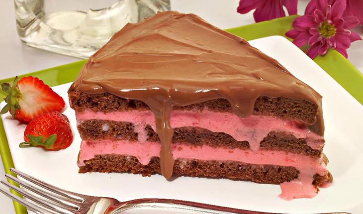Na foto há uma fatia de um bolo de chocolate com recheio de morango.