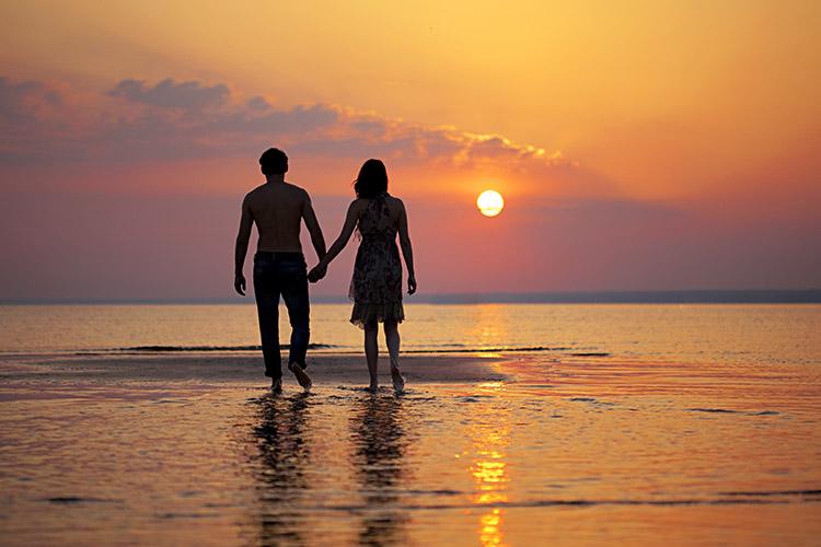 casal de mãos dadas andando no meio da água em uma praia