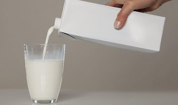 A foto mostra uma mão feminina colocando leite em um copo. Como uma fonte de cálcio, é importante incluir o leite na alimentação para prevenir dores nas costas na terceira idade