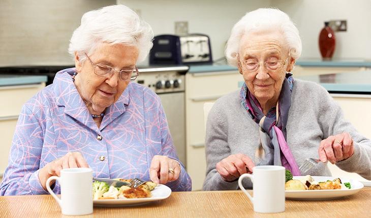 A foto mostra duas senhoras comendo juntas. Uma alimentação saudável é importante para evitar o Alzheimer