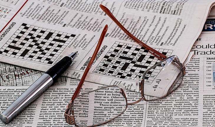A foto mostra um óculos e uma caneta em cima de um jornal na pa´gina das cruzadinhas. Esse tipo de jogo ajuda você a turbinar o cérebro