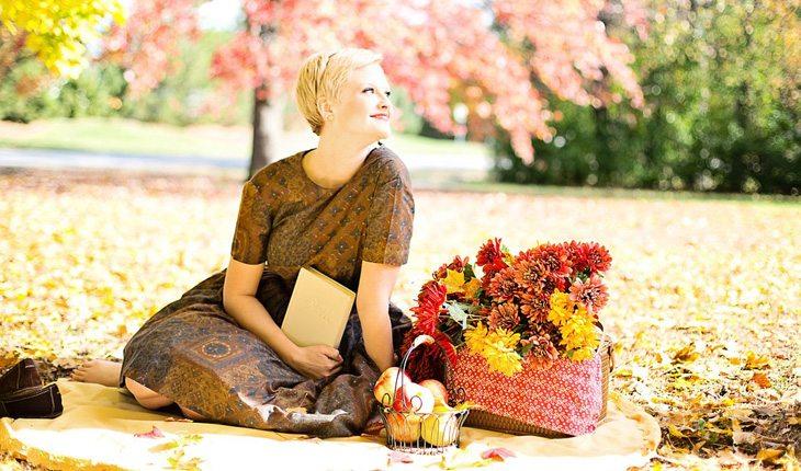 Dicas para relaxar. Na foto, uma mulher fazendo um piquenique. Ao lado dela uma cesta de flores